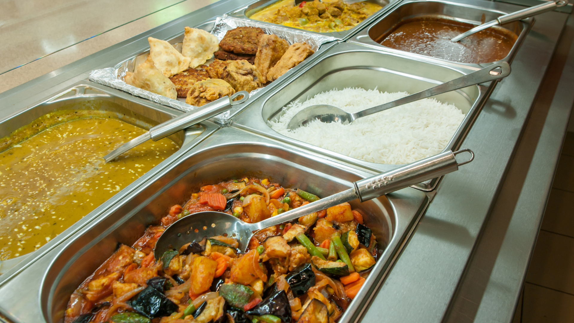 Buffet line with stainless trays of soups, rice, fried chicken, and stir-fried vegetables