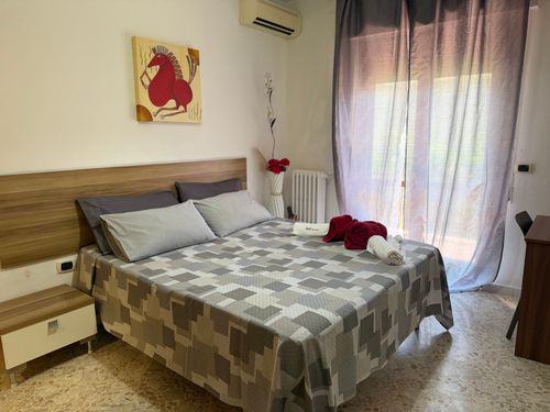 Camera da letto con due letti in legno, lenzuola bianche, quadri alle pareti e un letto a castello in un angolo.