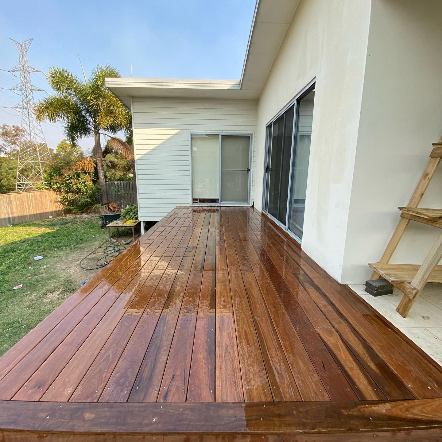 Wooden deck alongside a white house with a sliding glass door and a small garden.