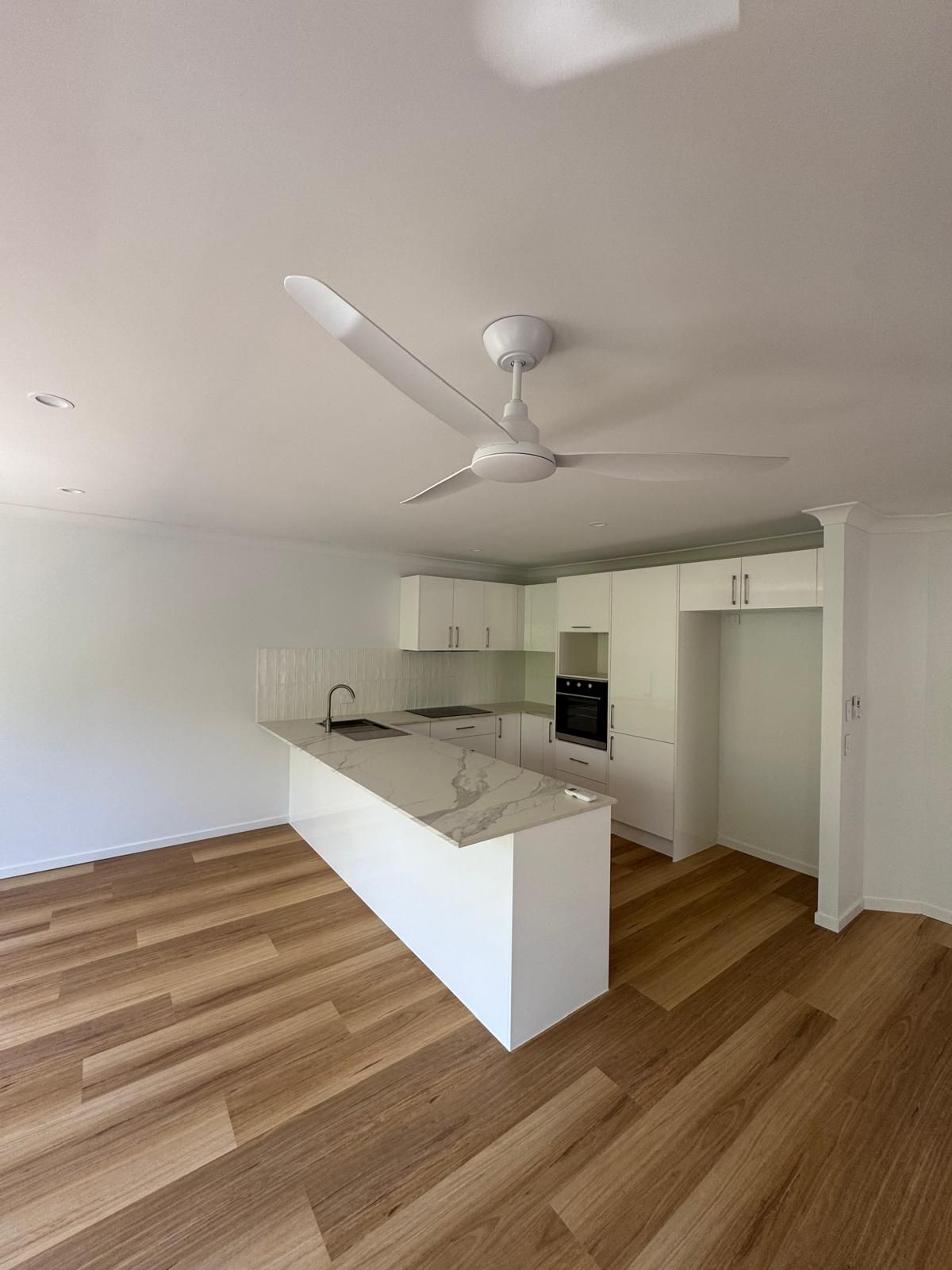 Modern kitchen with white cabinets, island, oven, and wood-look flooring. White ceiling fan.