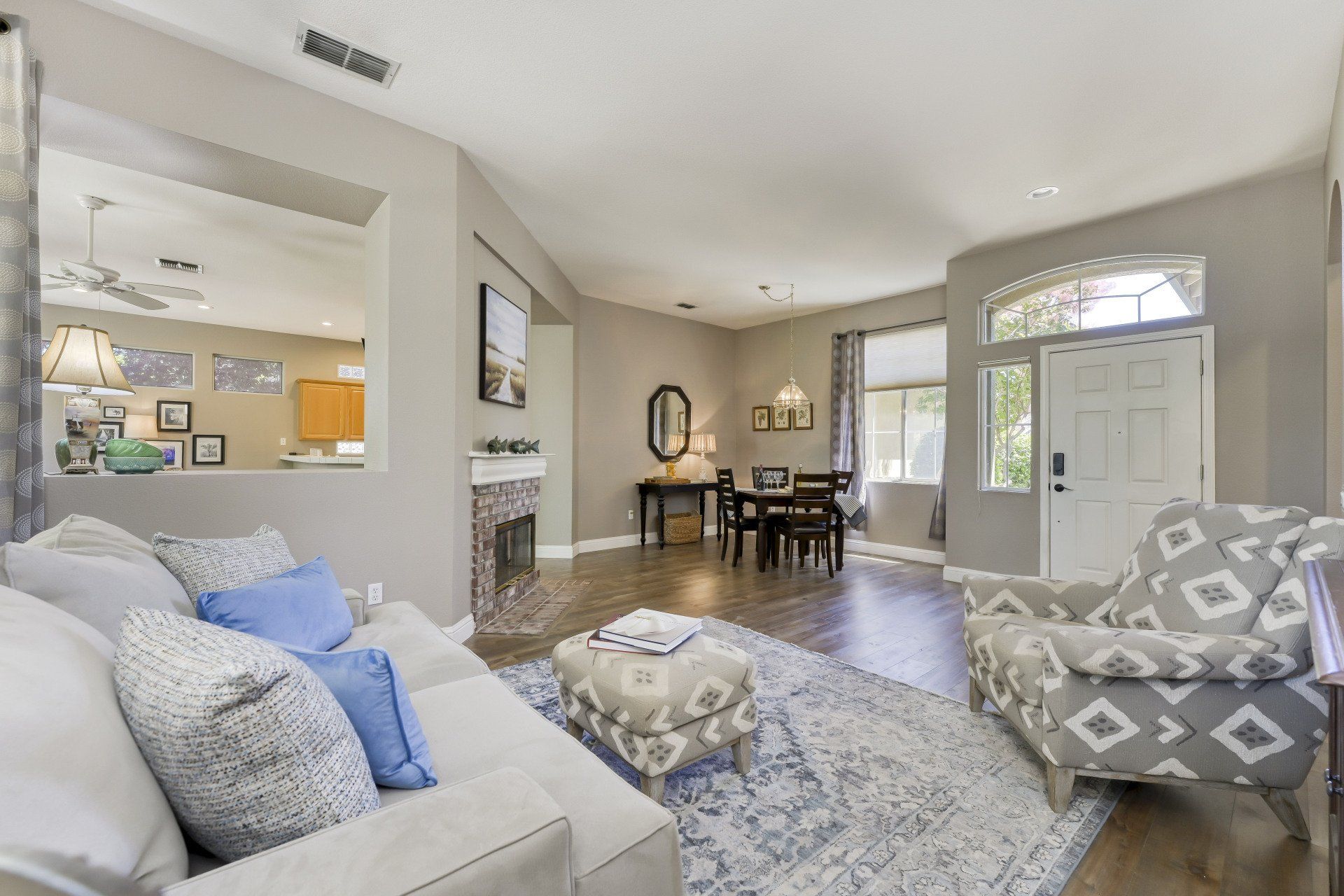 Living room with open floor plan, light gray walls, hardwood floors, sofa, patterned chair, and dining area.