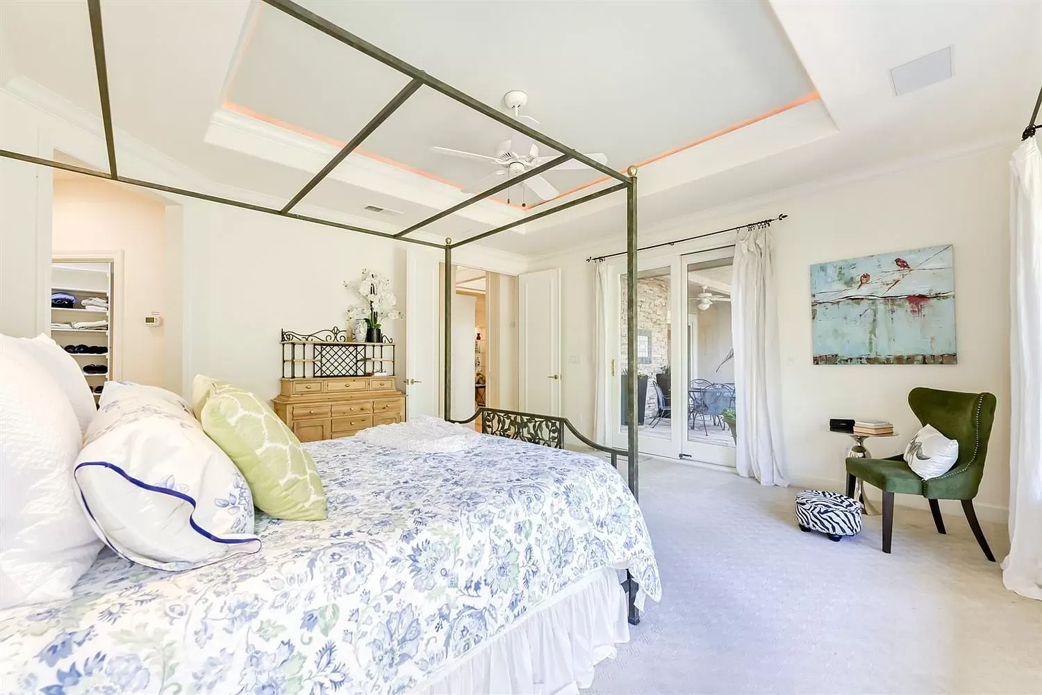 Spacious bedroom with a canopy bed, light blue bedding, and a green chair with a painting.