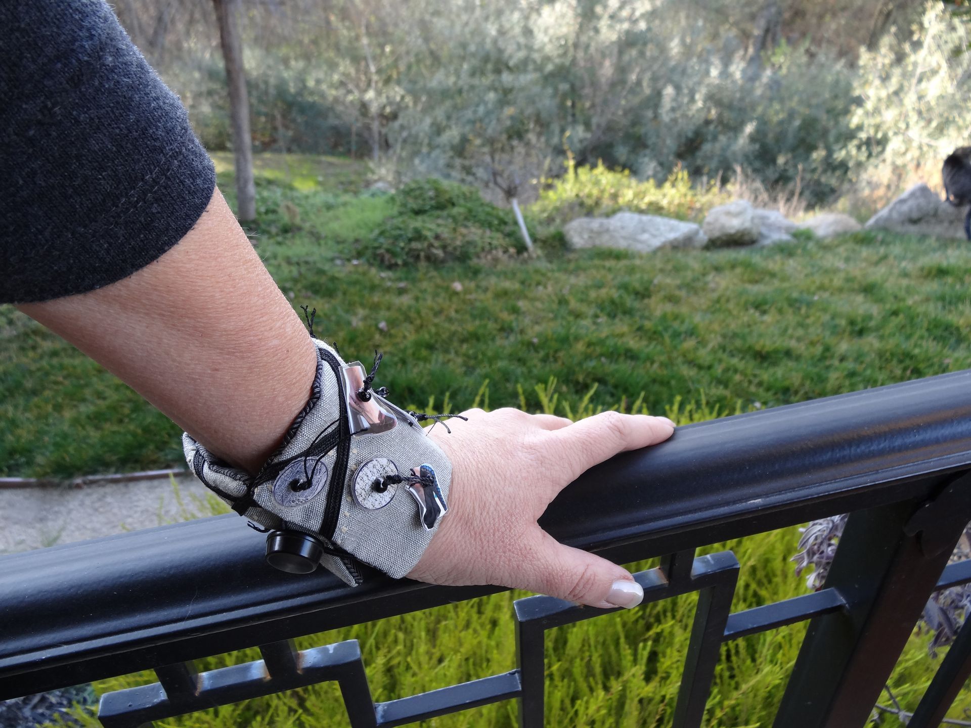 Woman's hand resting on a black railing, wearing a patterned silver and black bracelet.