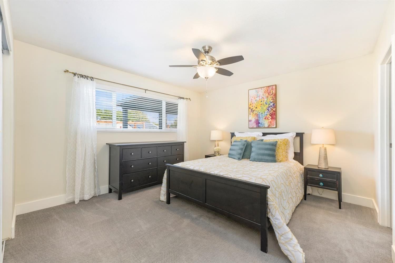 Bedroom with black bed, dresser, and nightstand, neutral walls, and a colorful painting.