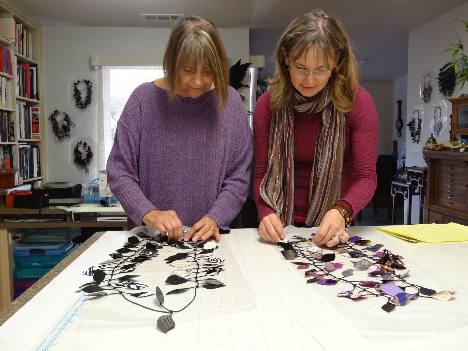 Marlene Heinz and Jonelle Tannahill are arranging jewelry on a table. One wears purple, the other burgundy. Indoor setting.