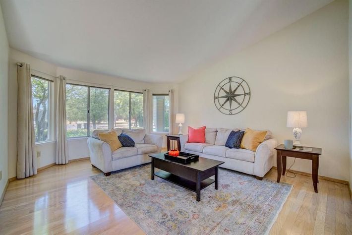 Bright living room with two sofas, coffee table, wall clock, lamp, and large windows.