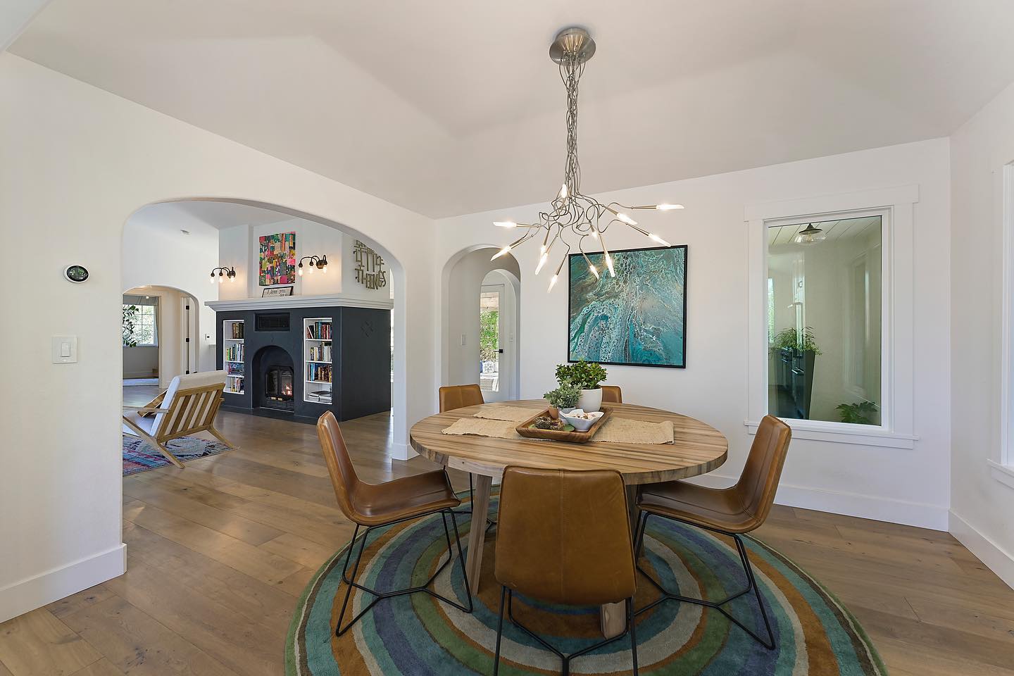 Dining room with round wooden table, chairs, colorful rug, and starburst chandelier.