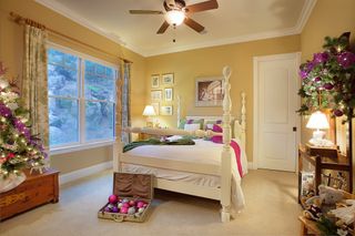 Holiday Decorating Cozy beige bedroom with a white bed, large window, ceiling fan, and floral decor