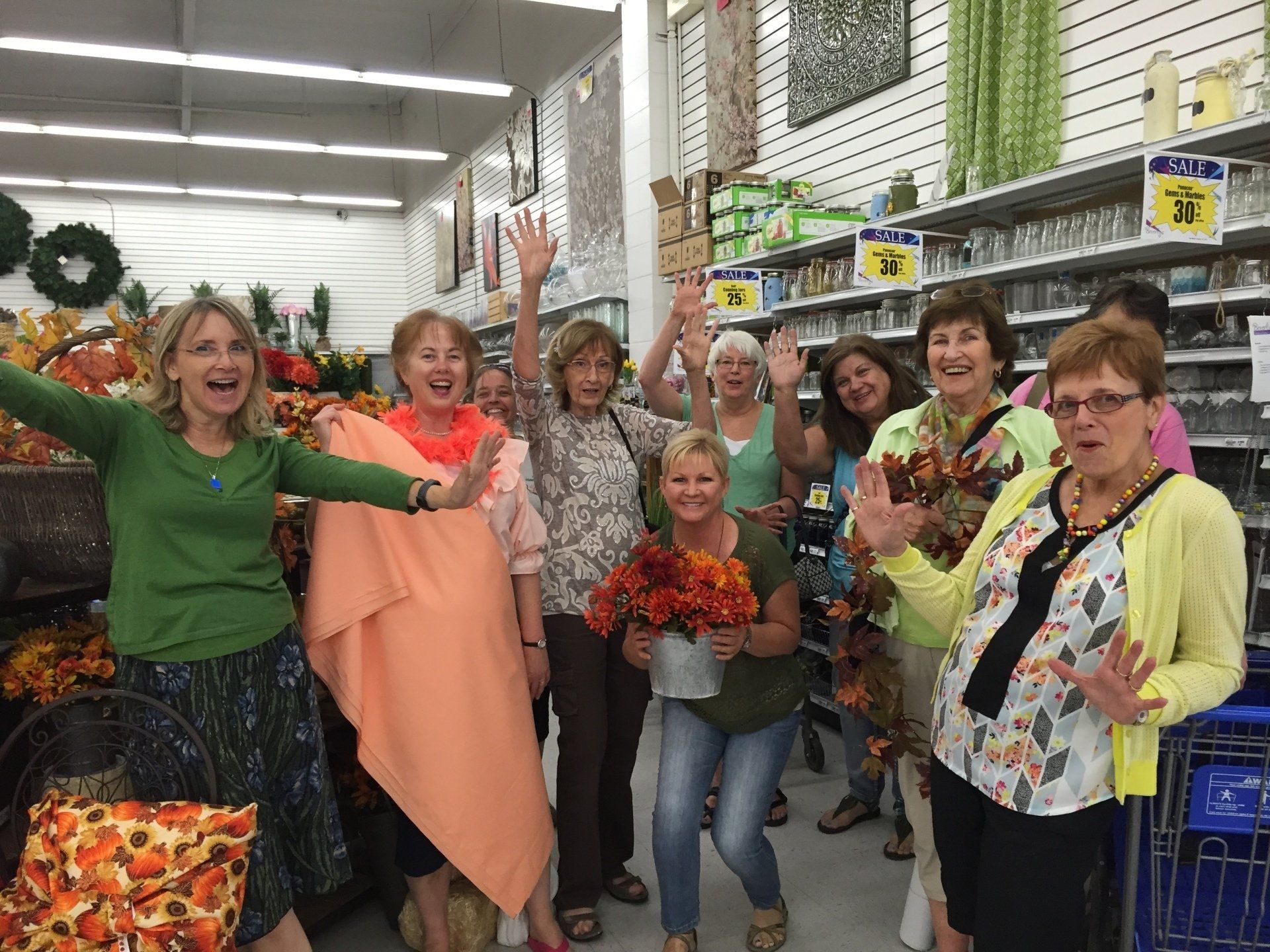Group of women shopping, waving in a store filled with autumn decorations.