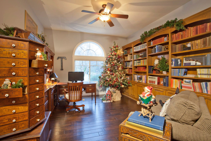 Cozy home office with Christmas decorations. A wooden desk and bookshelves are filled with books.