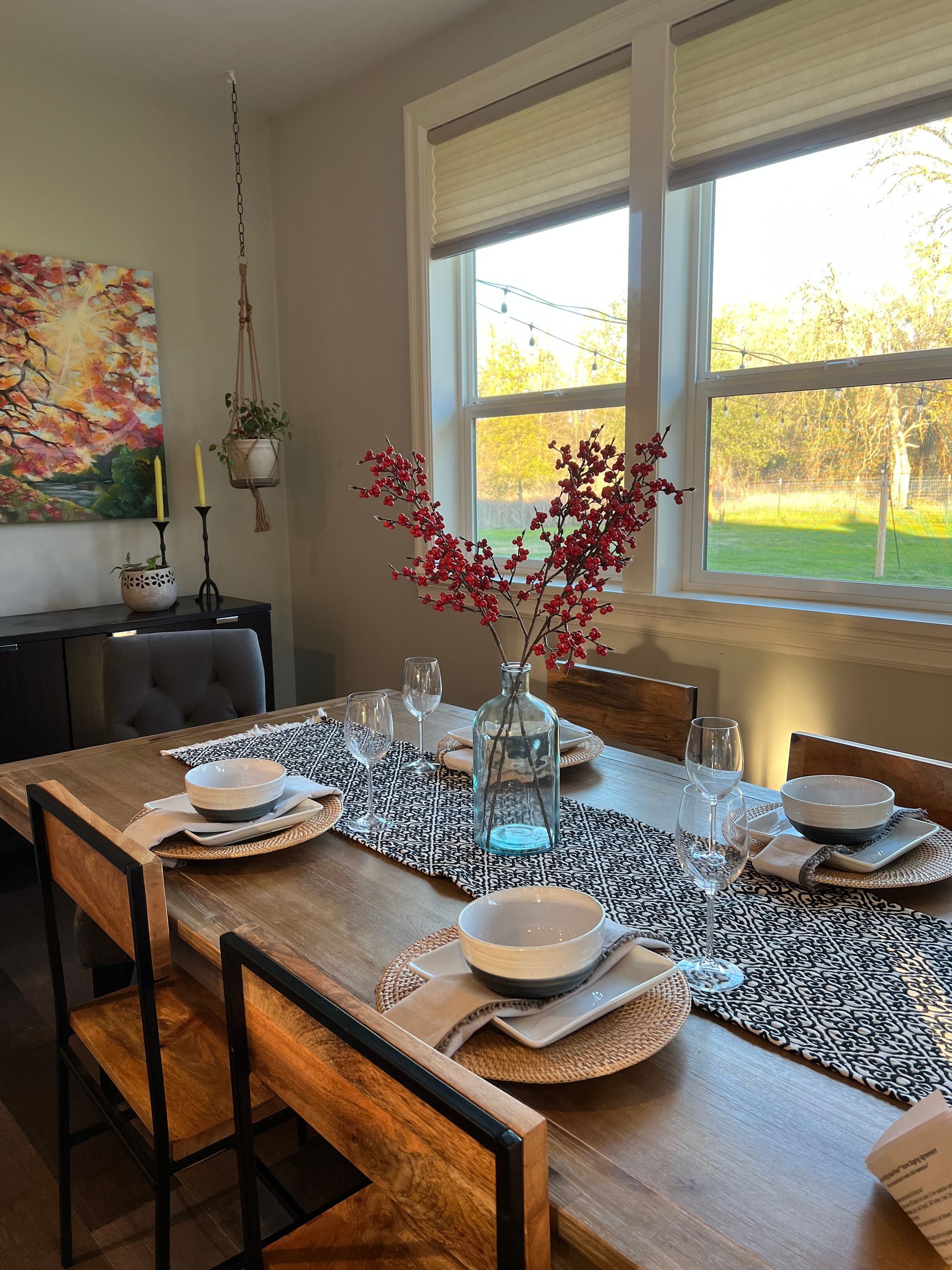 Dining room table set for meal; floral arrangement, sunlight, art, wood furniture.