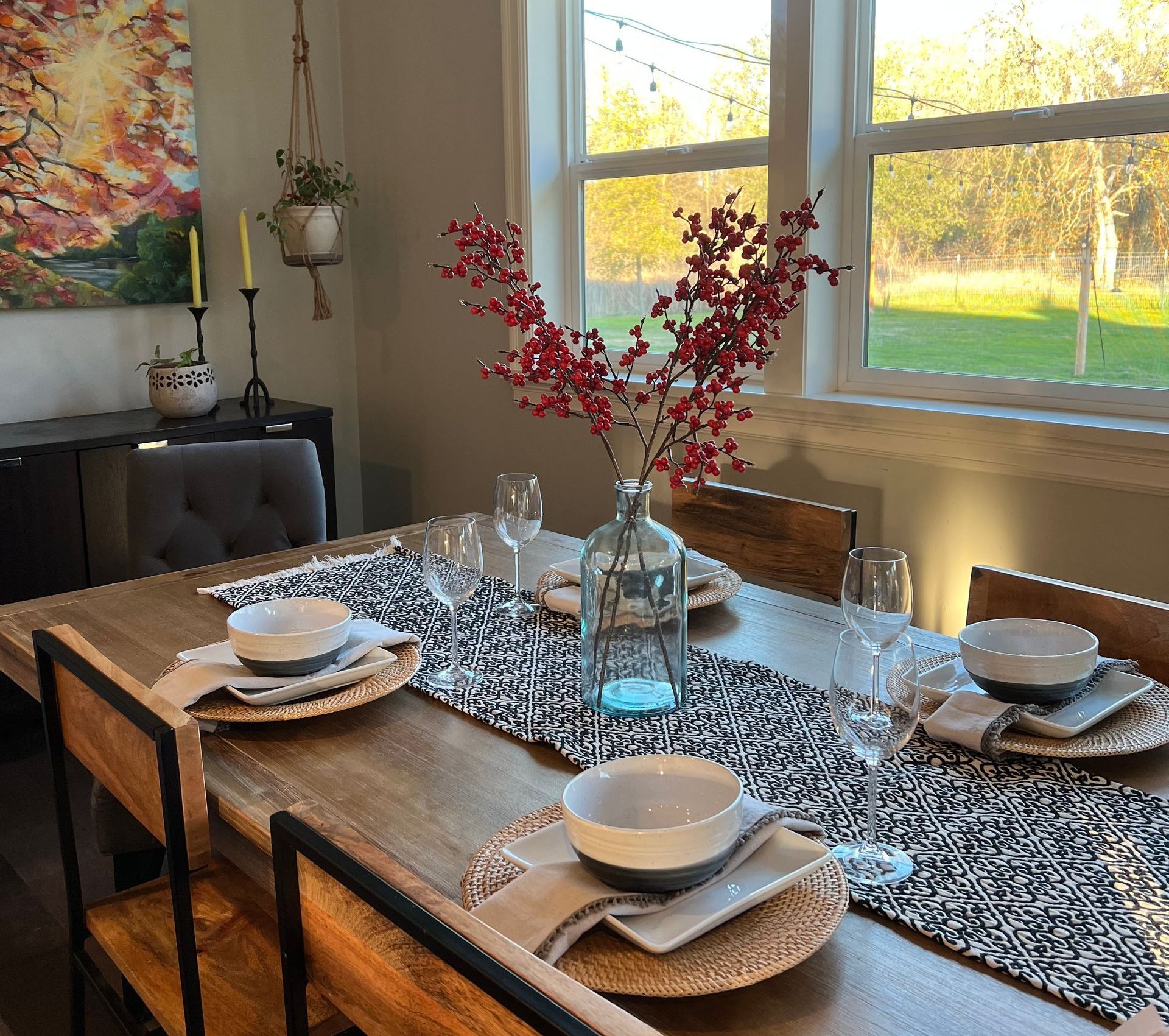 Dining table set for a meal with red berries in a vase, next to a window.