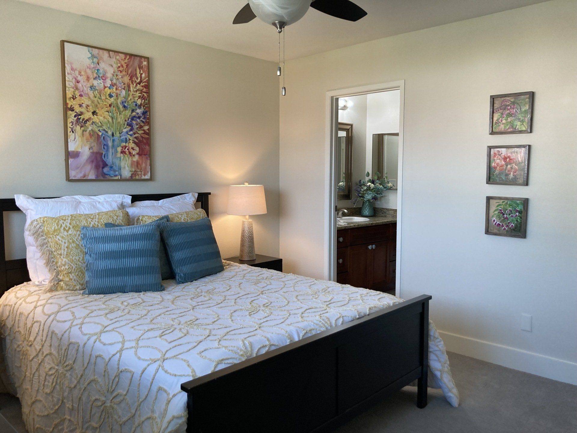 Bedroom with bed, artwork, and a bathroom entrance. White and blue bedding, floral painting.