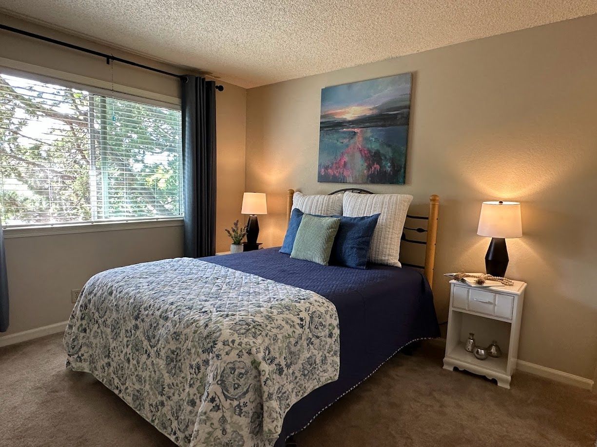 Bedroom with a bed, nightstands, window with blue curtains, and artwork.