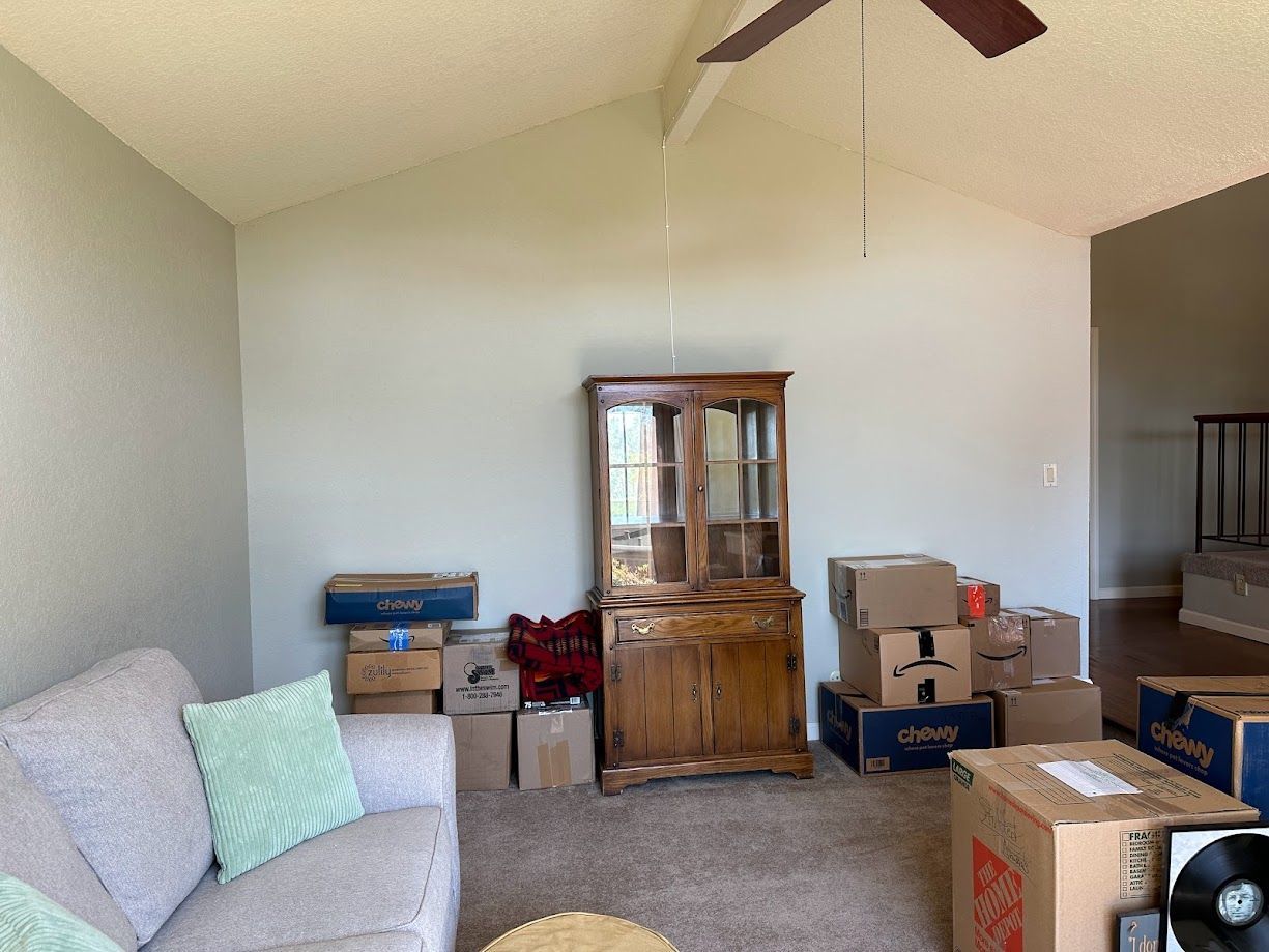 Living room with packed boxes, an old wooden cabinet, and a tan couch.
