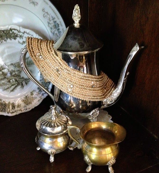 Silver teapot, brass cups, and decorative plate on a dark shelf.