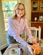 Woman arranging a pumpkin centerpiece on a dining table with lit candles and fall decor