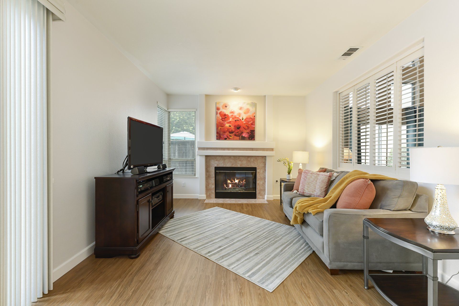 Living room with fireplace, TV, gray couch, rug, and artwork. White walls and wooden floors.