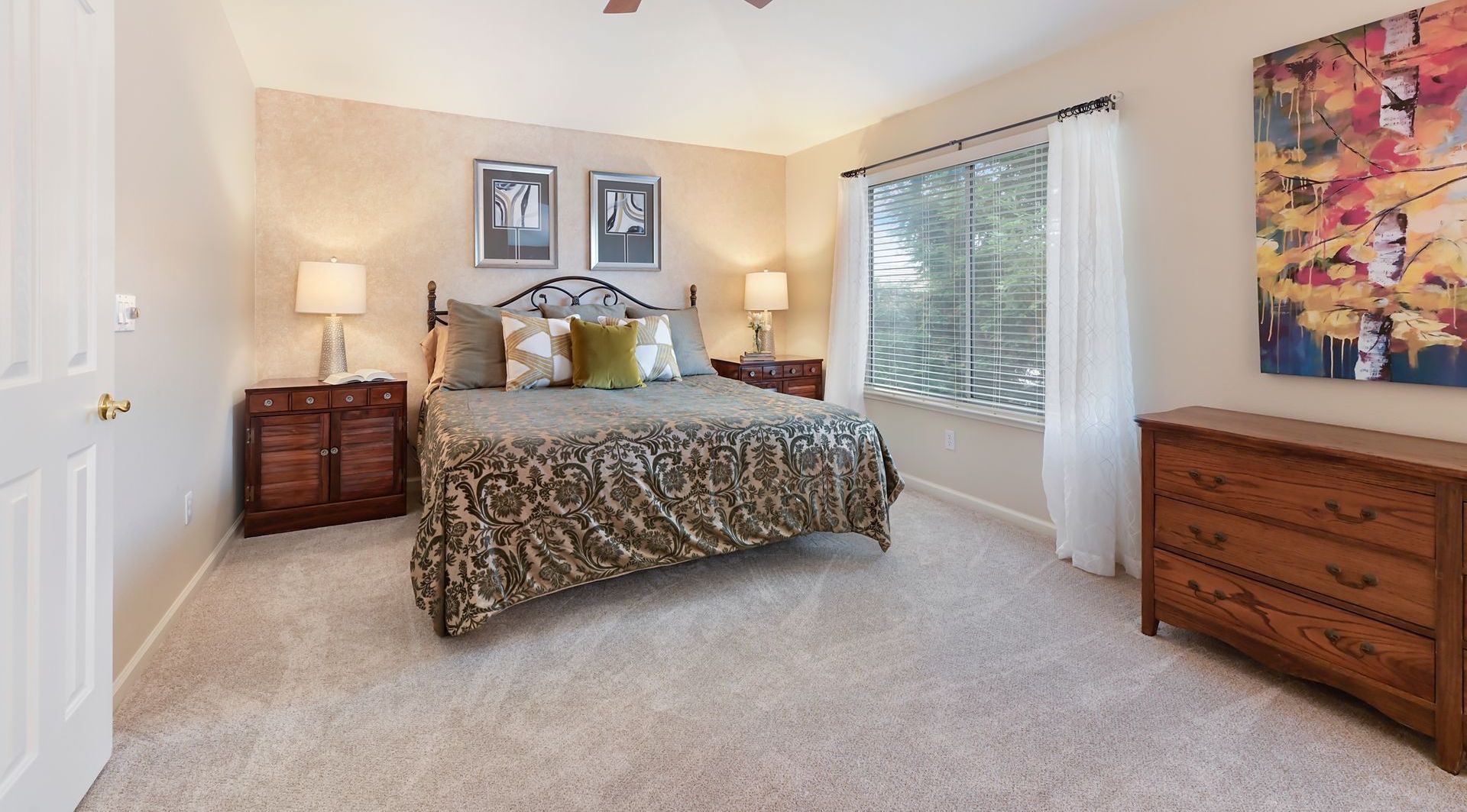 Bedroom with bed, nightstands, dresser, art, and window with white curtains.