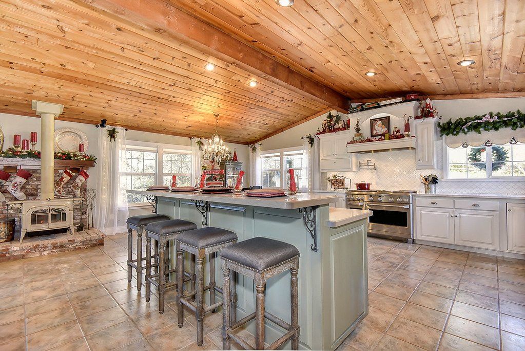 Rustic kitchen with wood ceiling, large island with stools, fireplace, and festive decorations.