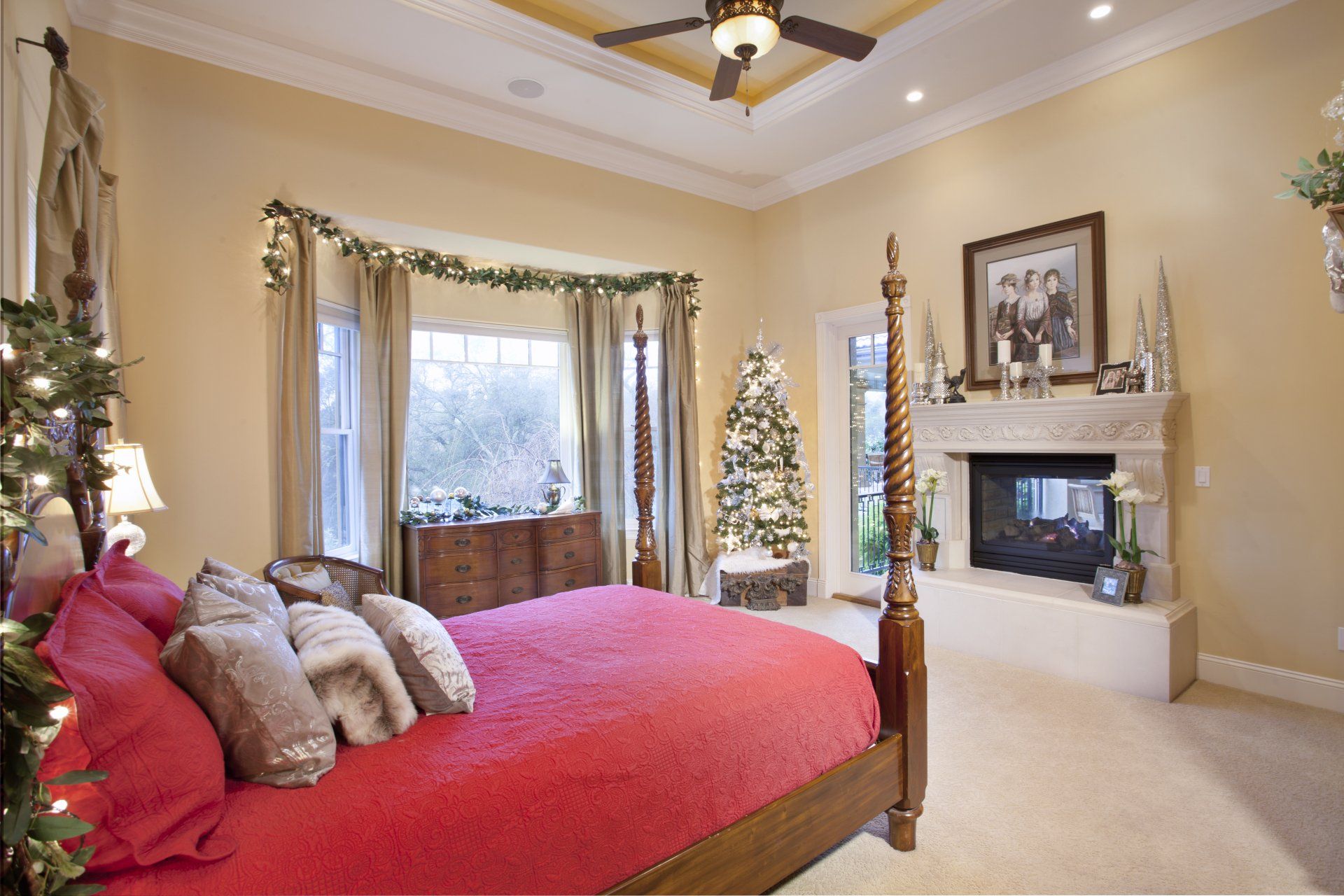 Bedroom decorated for Christmas; red bedding, Christmas tree, fireplace, window with garland.