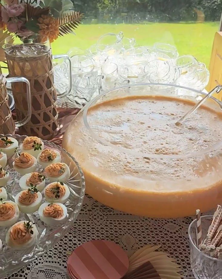 Deviled eggs, punch bowl, iced tea, and snacks on a table set outdoors.