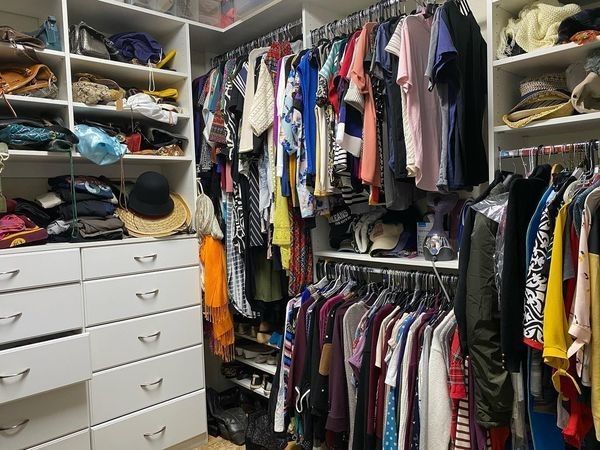Walk-in closet filled with clothes, shoes, and accessories. Shelves and drawers are white. Garments are brightly colored.