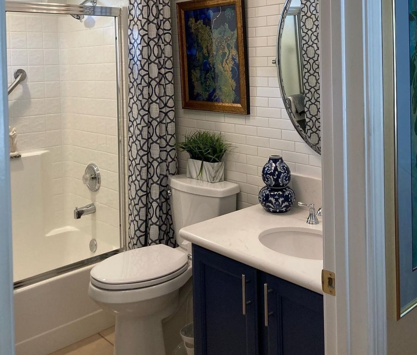Bathroom with white tiles, blue vanity, toilet, shower curtain, and wall art.