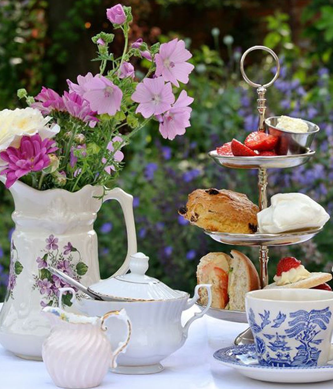 Afternoon tea set with flowers and tiered tray of treats outdoors.