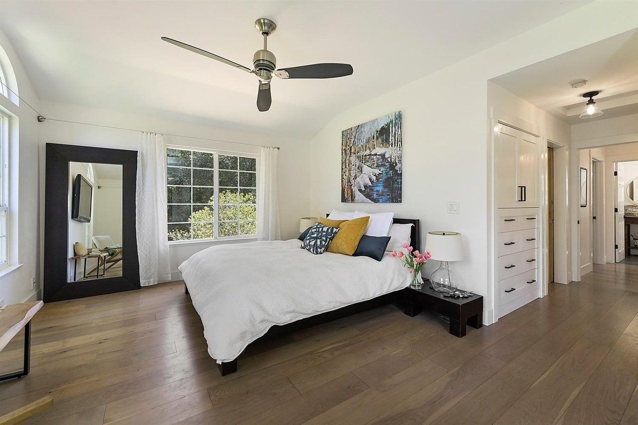 Bedroom with bed, large mirror, window, artwork, and hardwood floors.