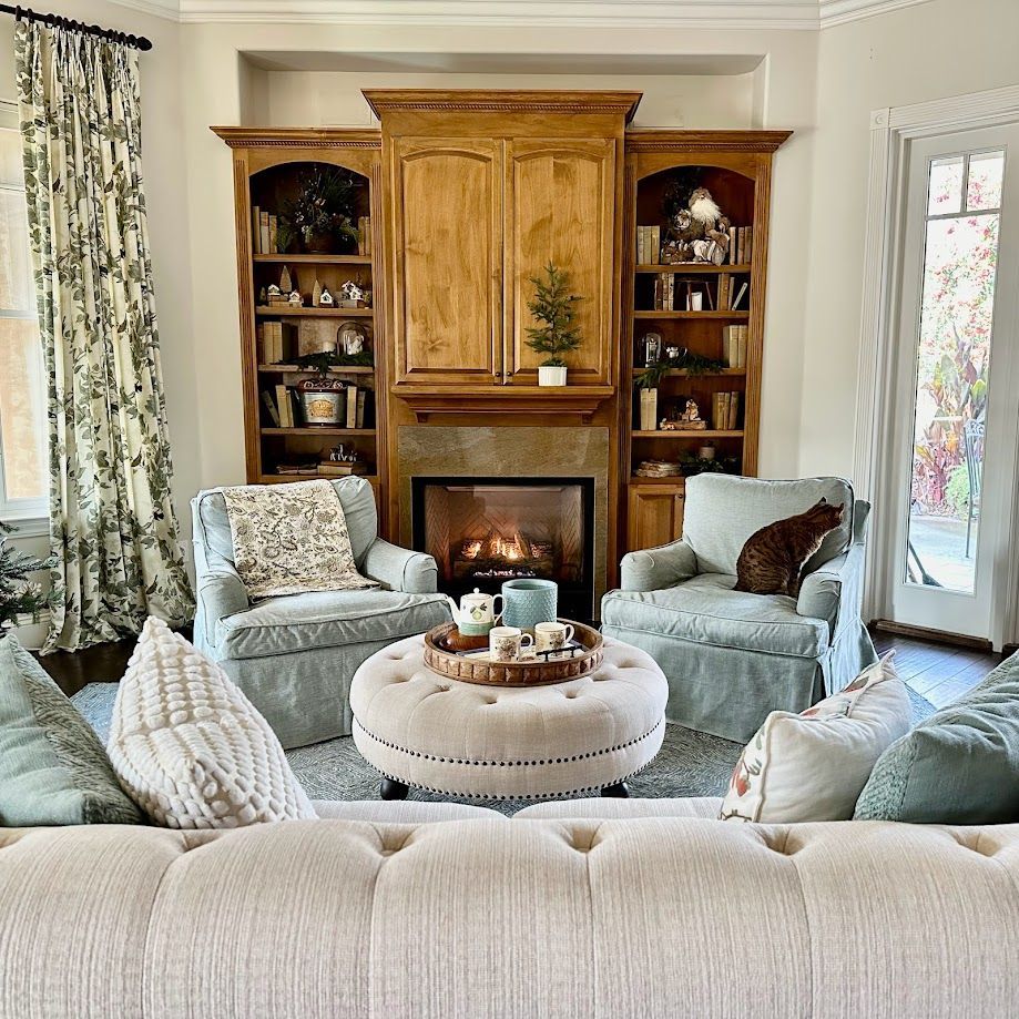 Cozy living room with built-in shelves around fireplace, two armchairs, and a tufted ottoman.