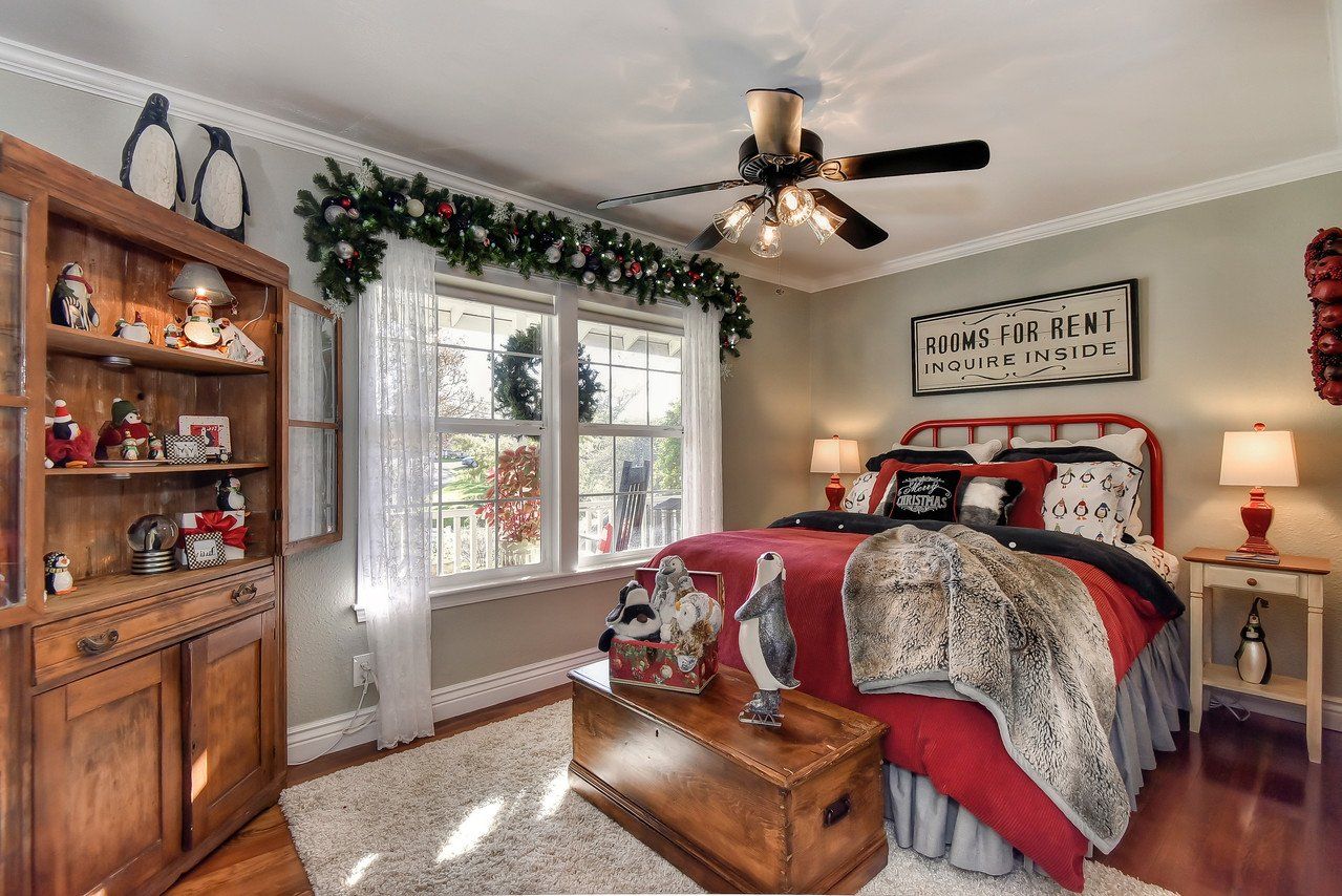 A decorated bedroom with red bedding, Christmas garland, a wooden trunk, and a hutch.
