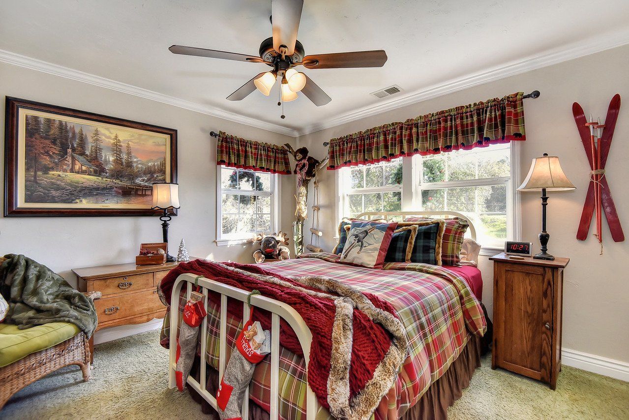 Cozy bedroom with a red and green plaid quilt, a landscape painting, and vintage decor.