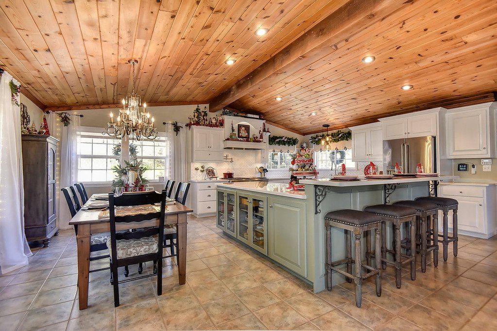 Kitchen with a wooden ceiling, island with seating, dining table, and white cabinets.