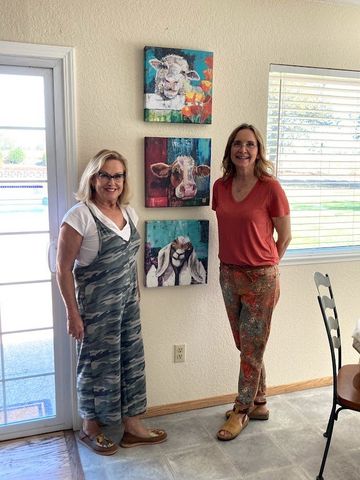 HGTV staging job Two women standing indoors beside three colorful wall photos in a bright room