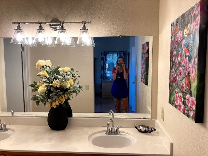 Bathroom vanity with mirror, flowers, and a person visible in the doorway reflection