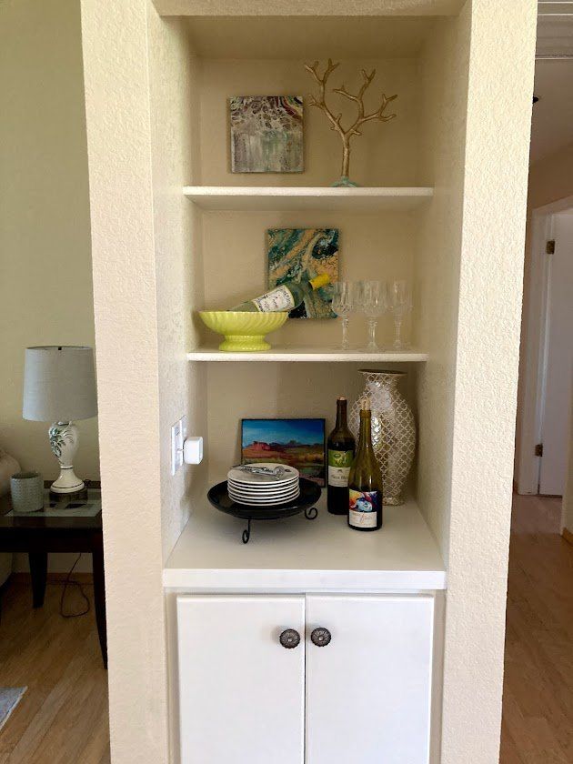 Built-in niche shelf with decor, bowls, glasses, and cabinet doors in a hallway alcove.