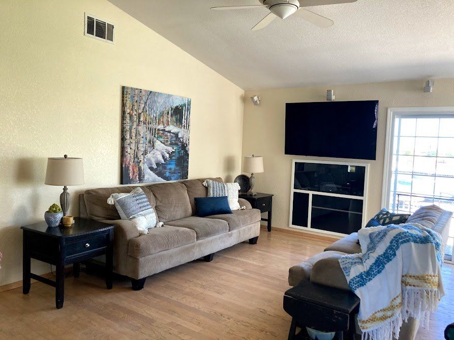Living room with beige walls, brown sofa, large TV, artwork, and a recliner with a blanket.