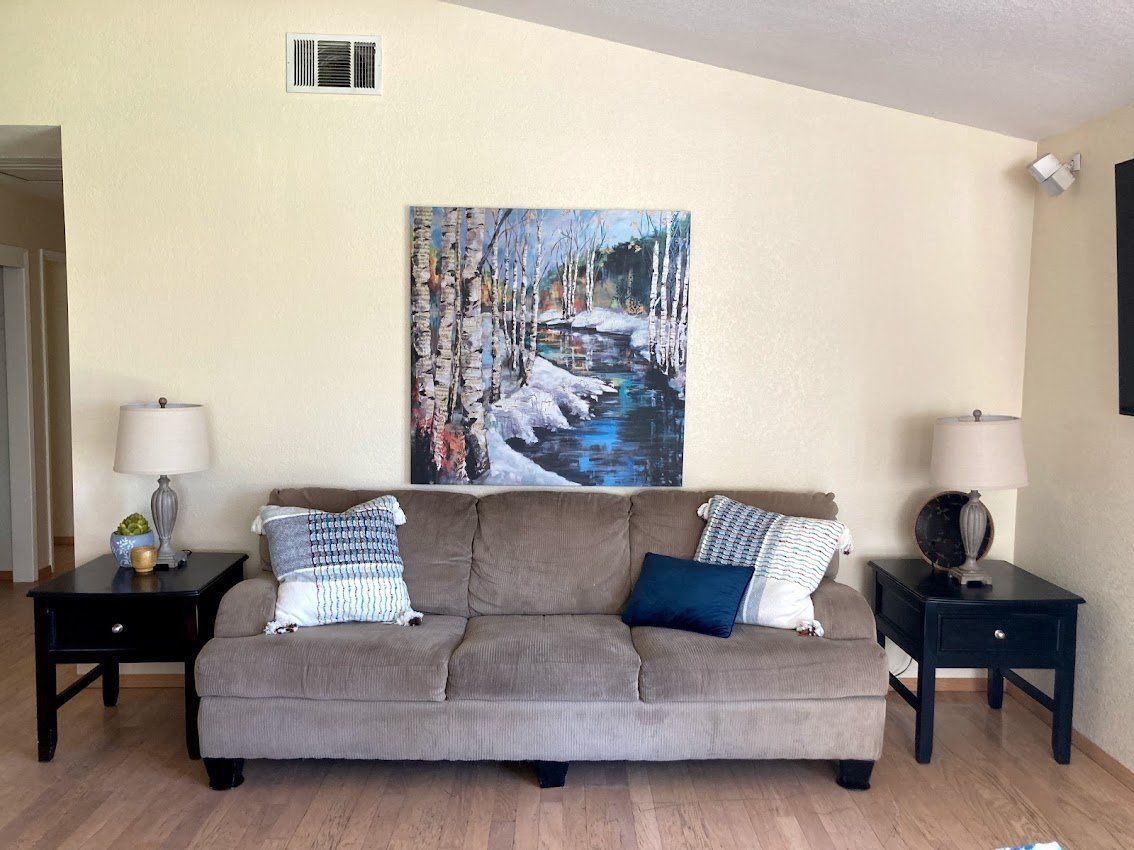 Living room with a brown couch, black end tables, and a painting above the couch.