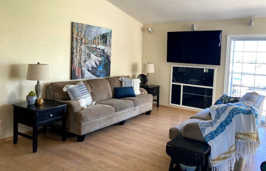 Living room with a couch, TV above a cabinet, and a recliner. Beige walls, light wood floor.