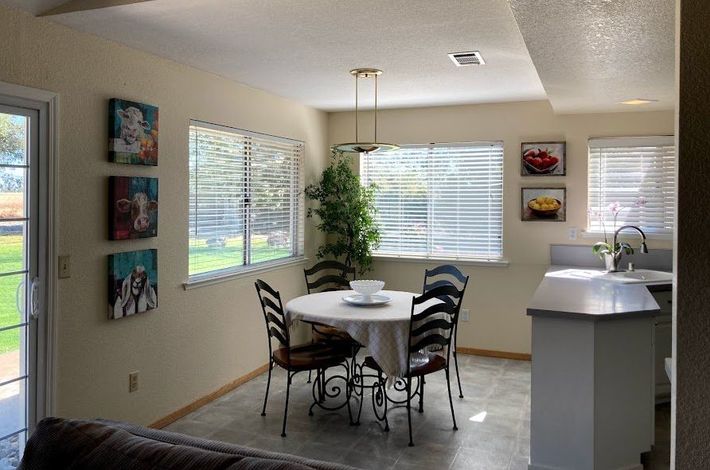 Bright dining area with round table, chairs, wall art, large windows, and a breakfast bar.