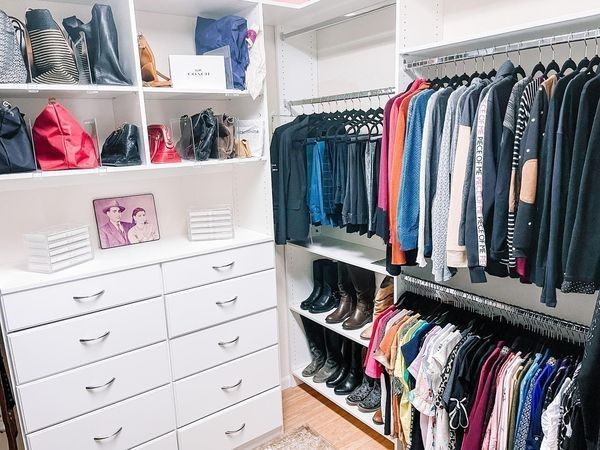 Walk-in closet with organized clothes, shoes, and purses. White shelving and drawers.