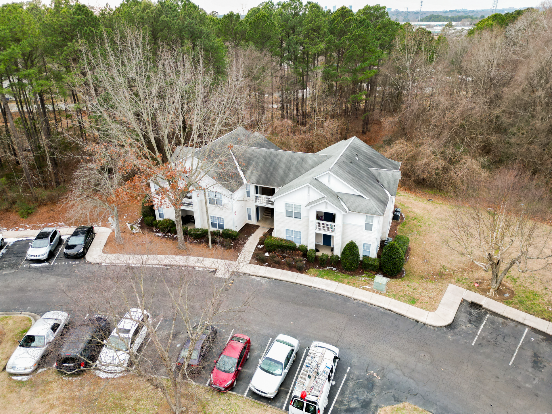 Apartment building surrounded by trees, with parked cars in front.