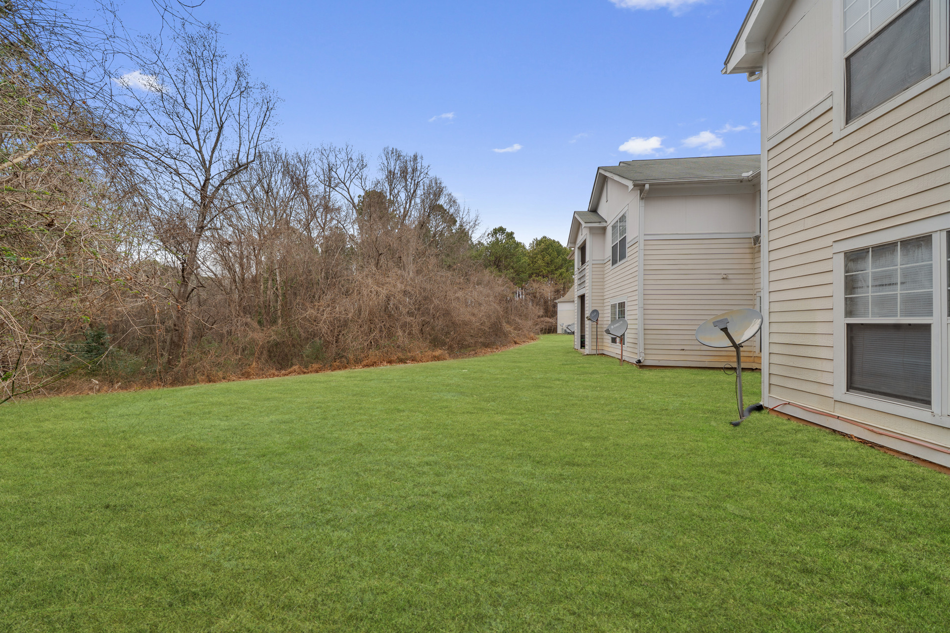 Green lawn next to a light-colored two-story building. Trees and a blue sky in the background.