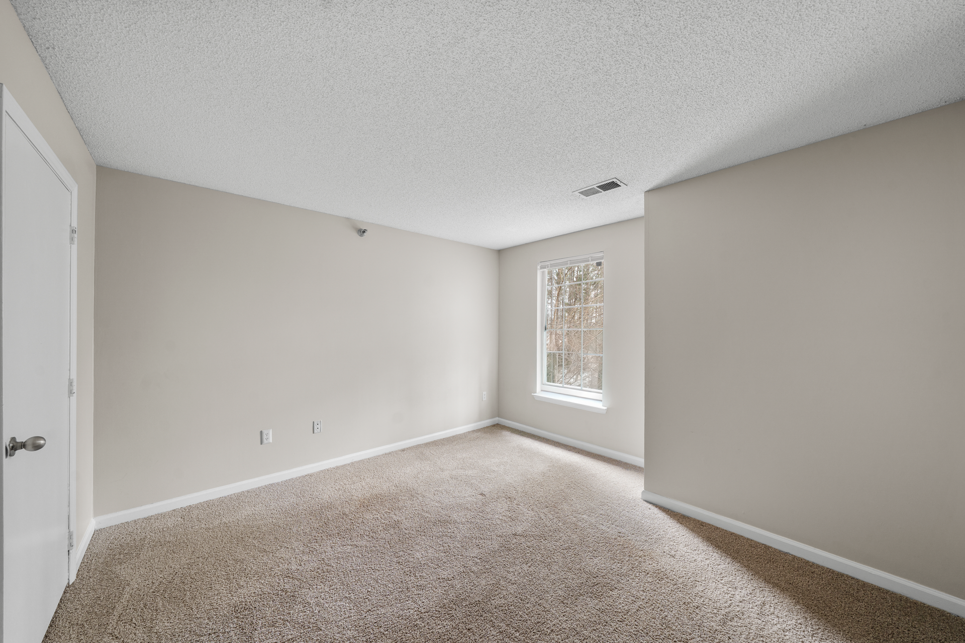 Empty room with beige walls, carpet, and a small window with a white frame.