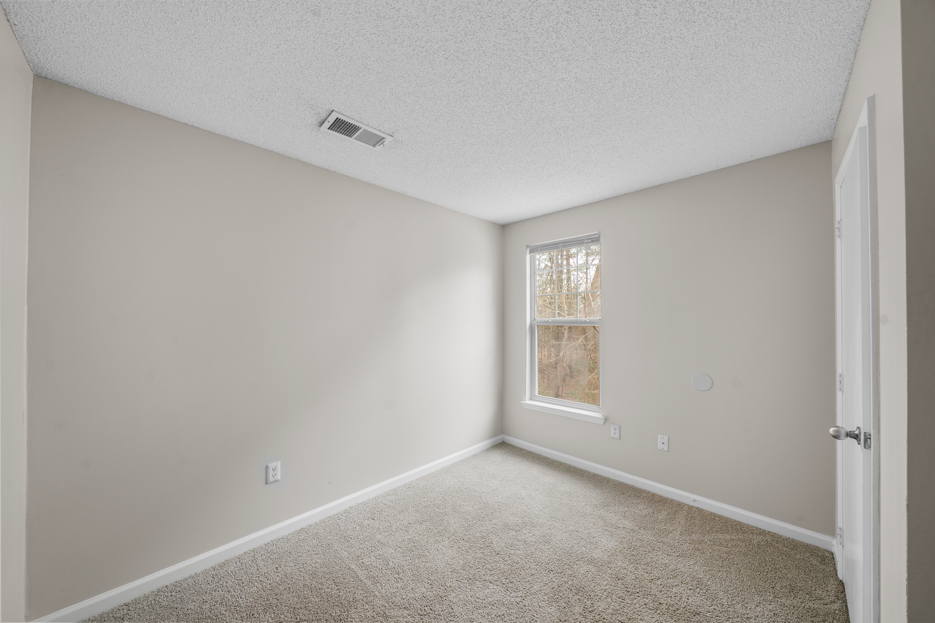Empty room with beige walls, patterned carpet, window, and white door.