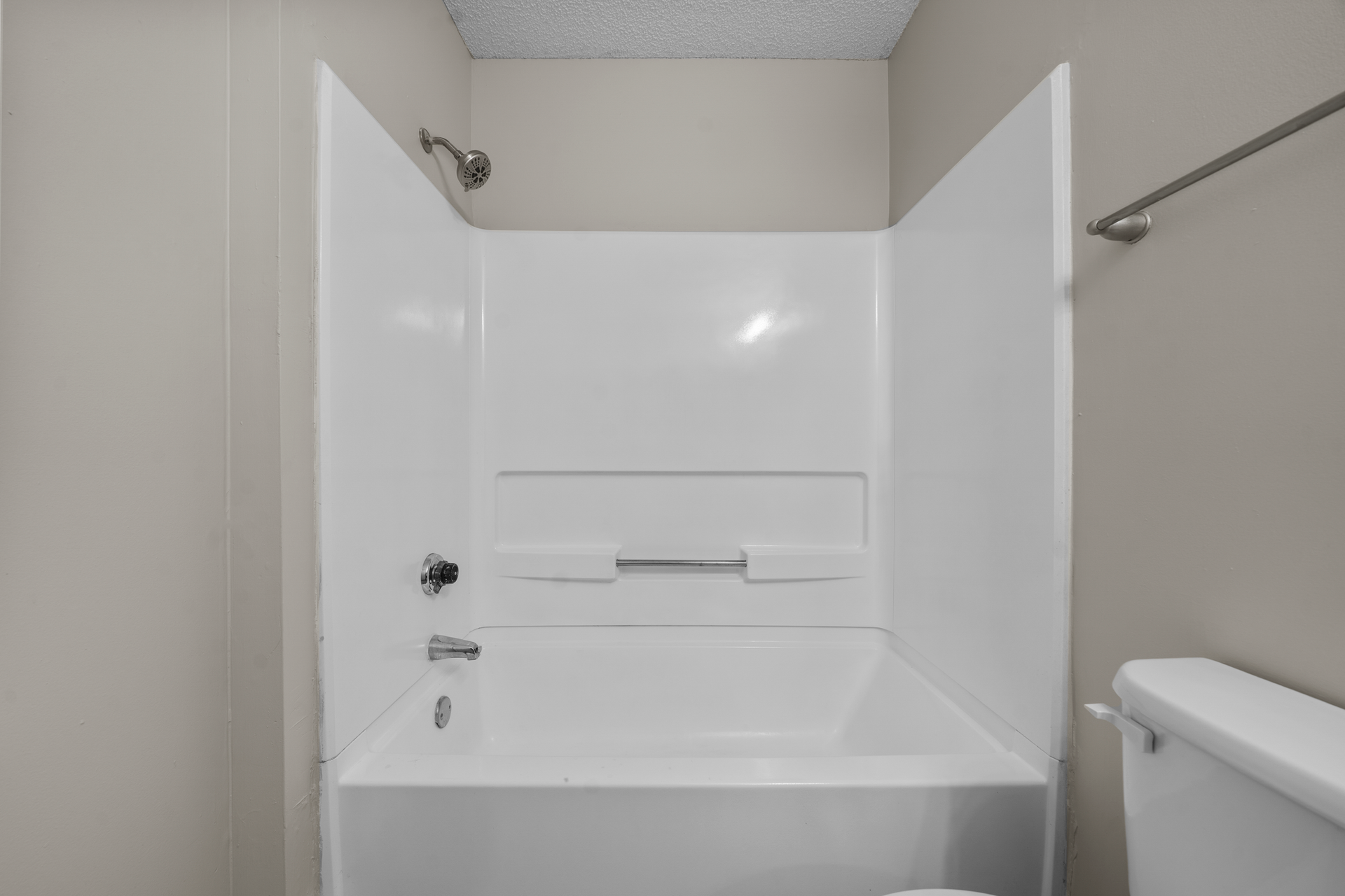 White bathtub and shower surround in a bathroom with a gray wall and a silver showerhead.
