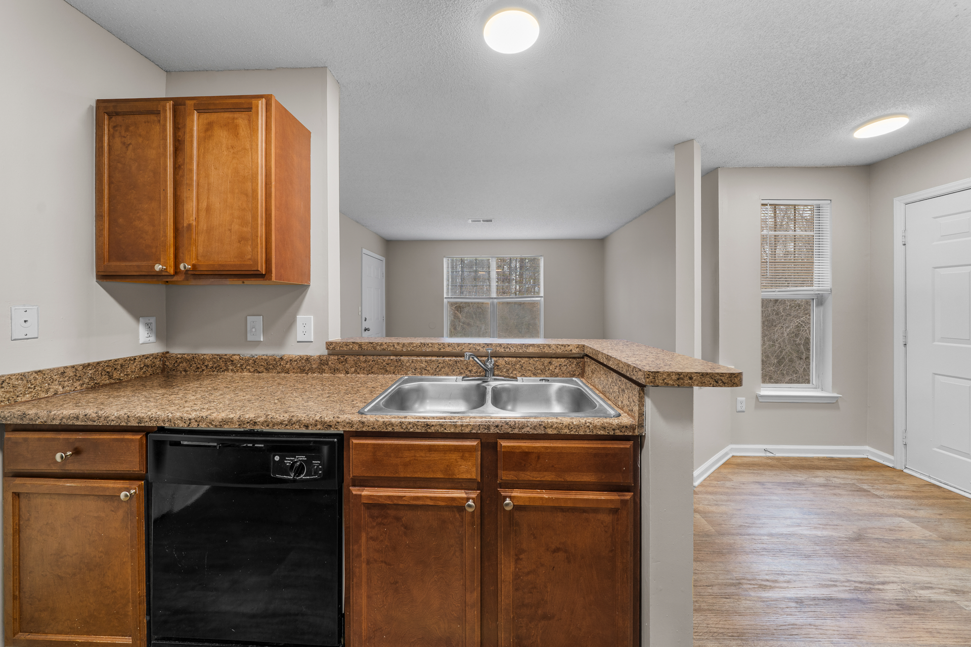 Kitchen with brown cabinets, granite countertops, and black dishwasher, overlooking living room.