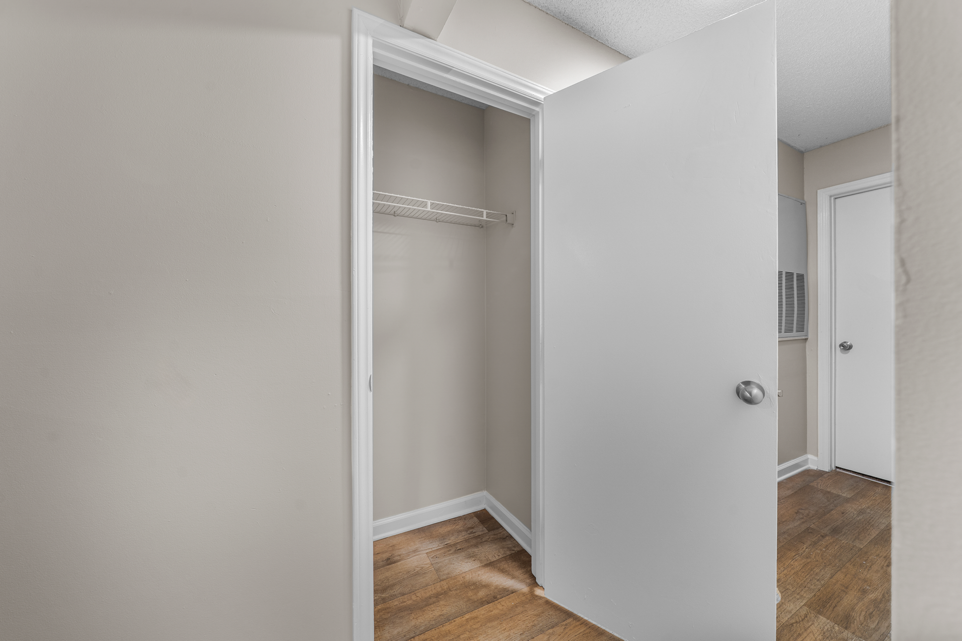 Open white closet door, beige walls, and brown floor.