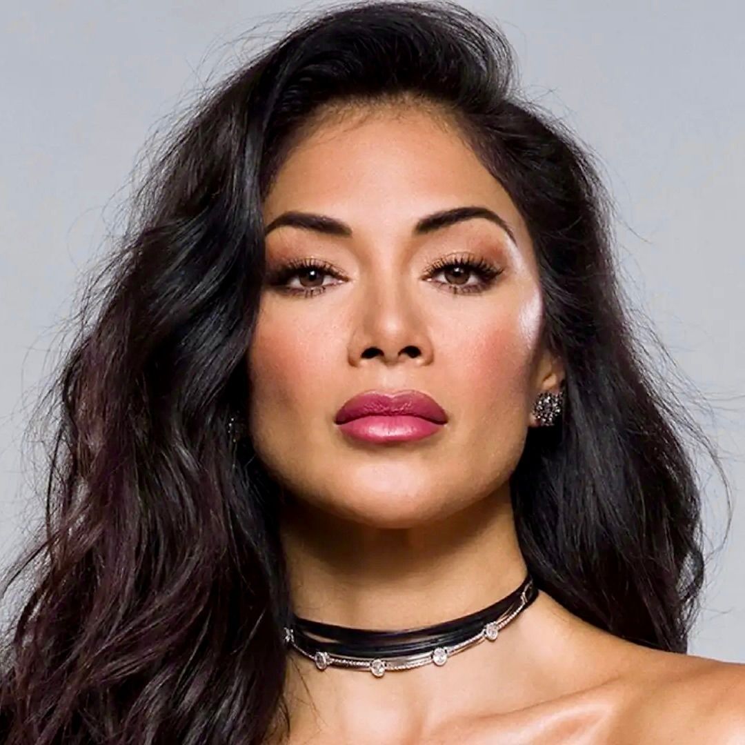 A headshot of Nicole Scherzinger, looking directly at the camera with a neutral expression, wearing a beaded choker.